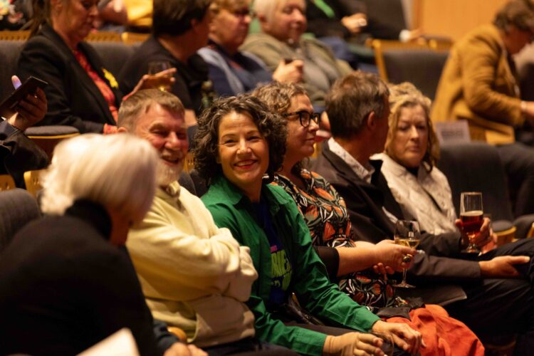 An audience member smiles at her friends. She wears a green cardigan. 